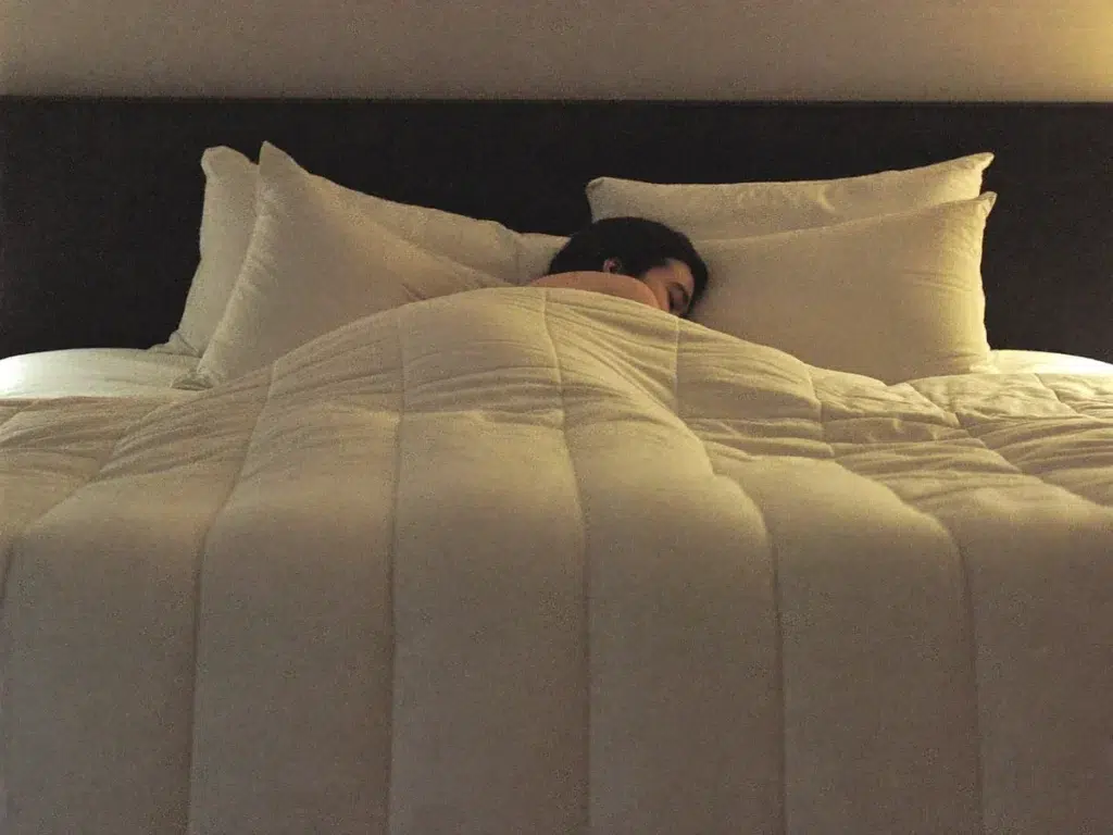 Massage for Jet Lag and Travel Fatigue: Does It Help? A traveler sleeping peacefully in a comfortable hotel bed after a relaxing evening massage