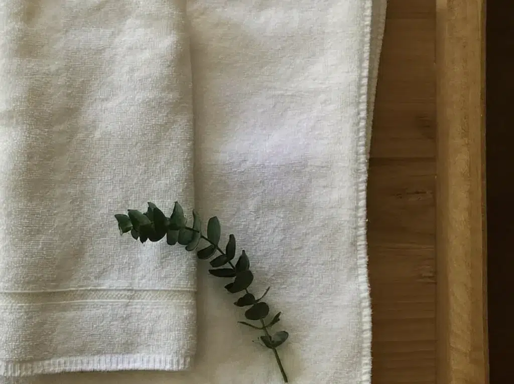 Oil on Hotel Sheets? How Outcall Massage Protects Your Bedding A massage oil bottle and neatly folded white towels arranged on a clean surface