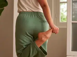 A person in casual clothing gently stretching their lower back at home near a window