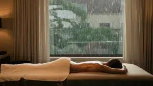 A relaxing oil massage in a warm hotel room with rain streaking down the window behind